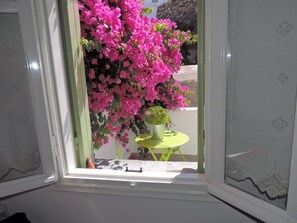 Una ventana con vistas a flores rosadas y una pequeña mesa con una planta en maceta.