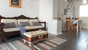A cozy living room with a wooden sofa, a striped rug, and a vintage suitcase coffee table. - Skaris Homes (Tinos)