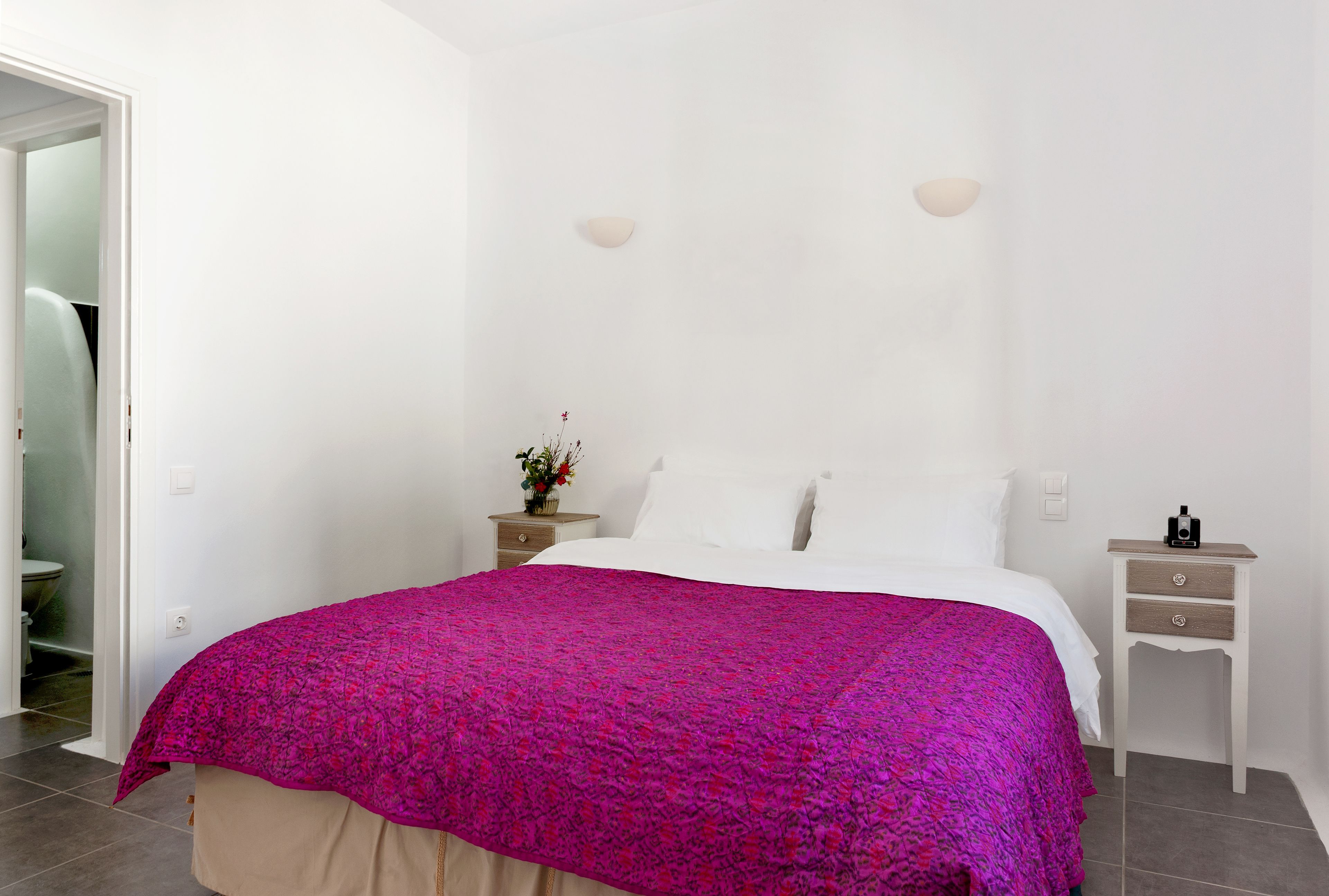 A bedroom with a bed, white walls, a nightstand, and a small table with a lamp.