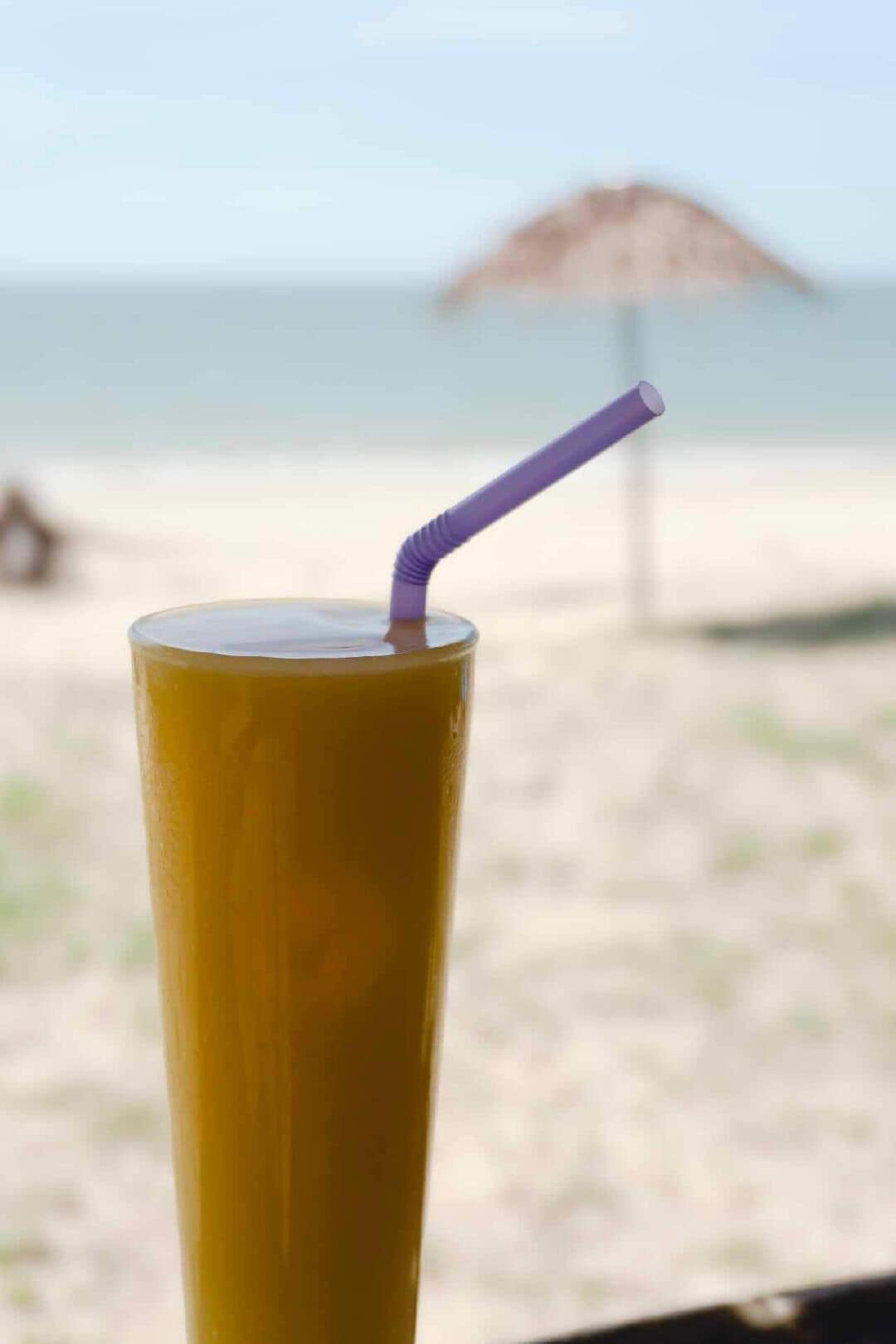 A tall glass with a straw, set against a beach backdrop.