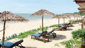 A beach with wooden lounge chairs and thatched umbrellas, a wooden deck, and a view of the ocean. - Pranee Beach Bungalows (Takua Pa)