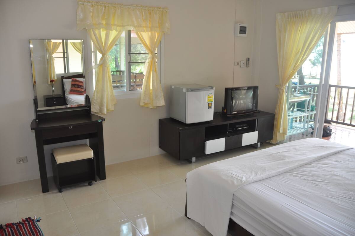 Quarto de hotel com cama, escrivaninha com cadeira, televisão e janela com cortinas.
