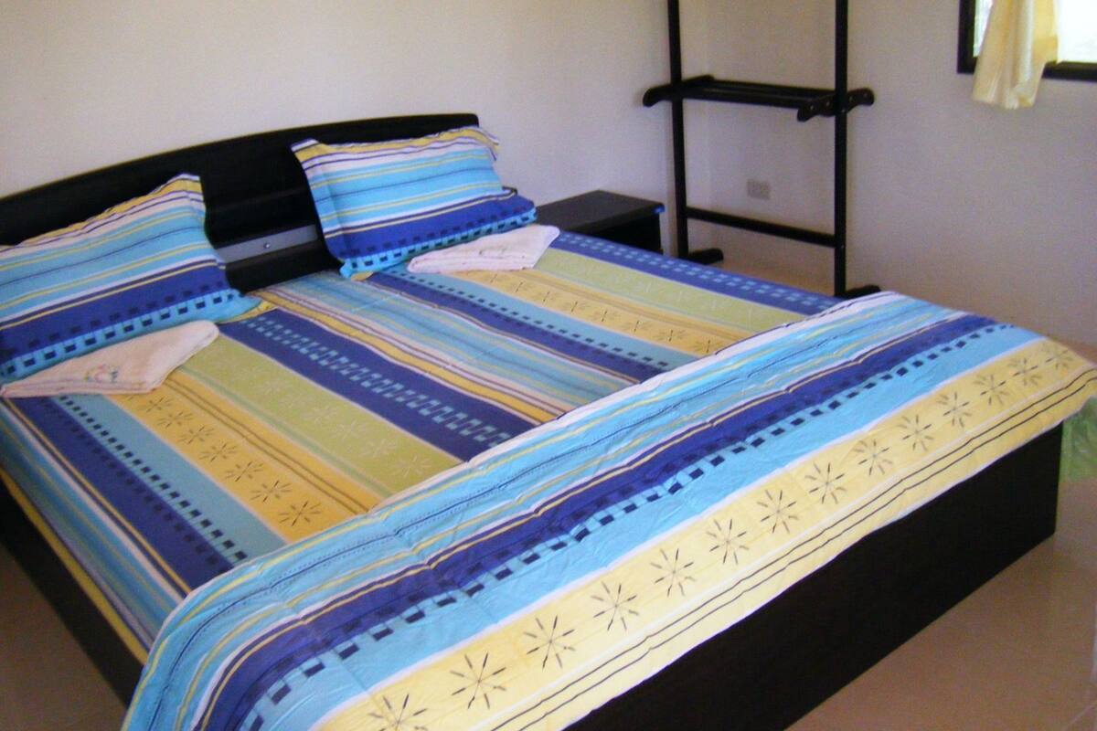 Uma cama com roupa de cama listrada, uma cabeceira preta e uma mesa de cabeceira com uma luminária.