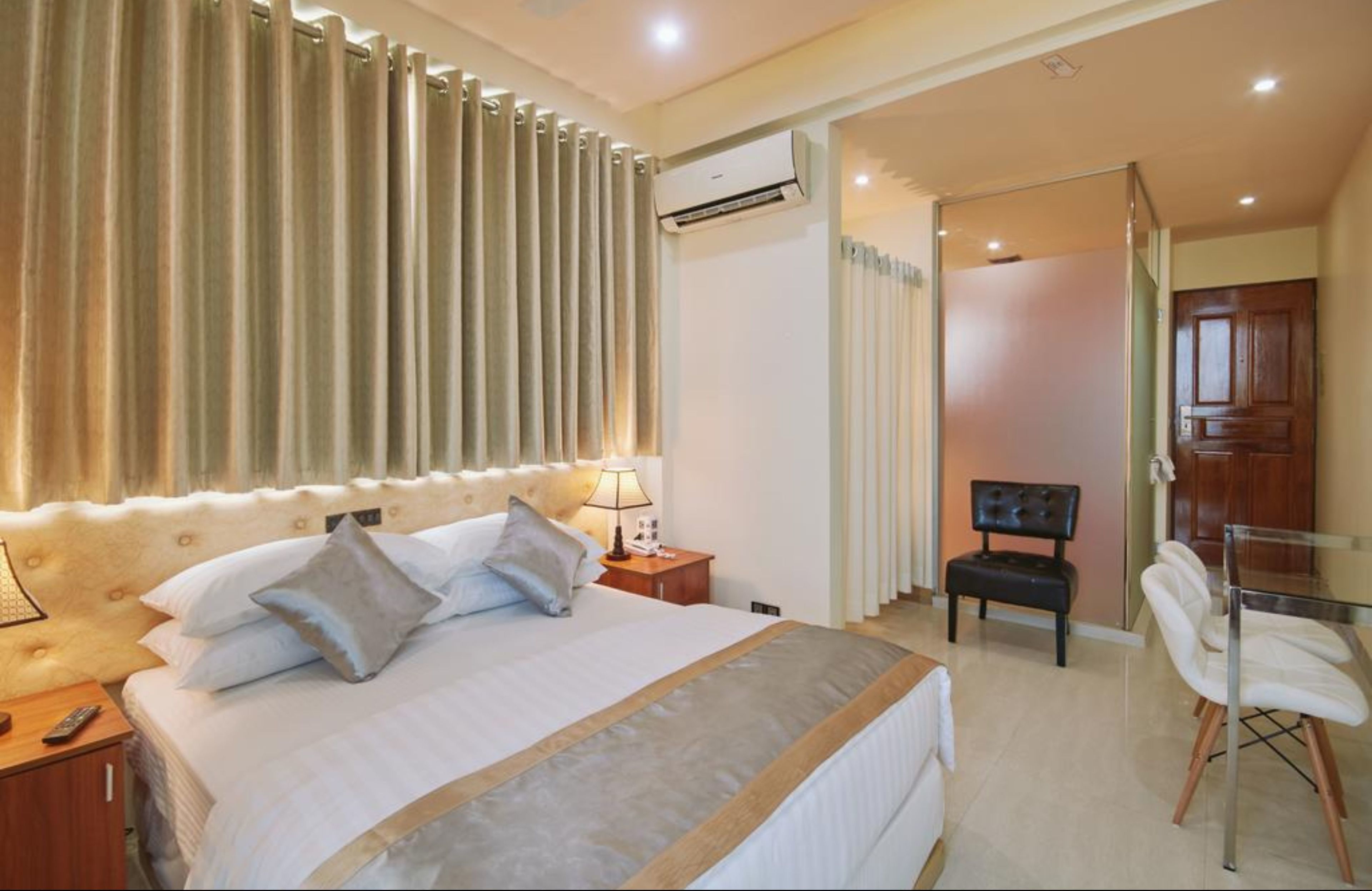 A hotel room with a large bed, a bedside table with a lamp, a chair, and a desk with a chair.