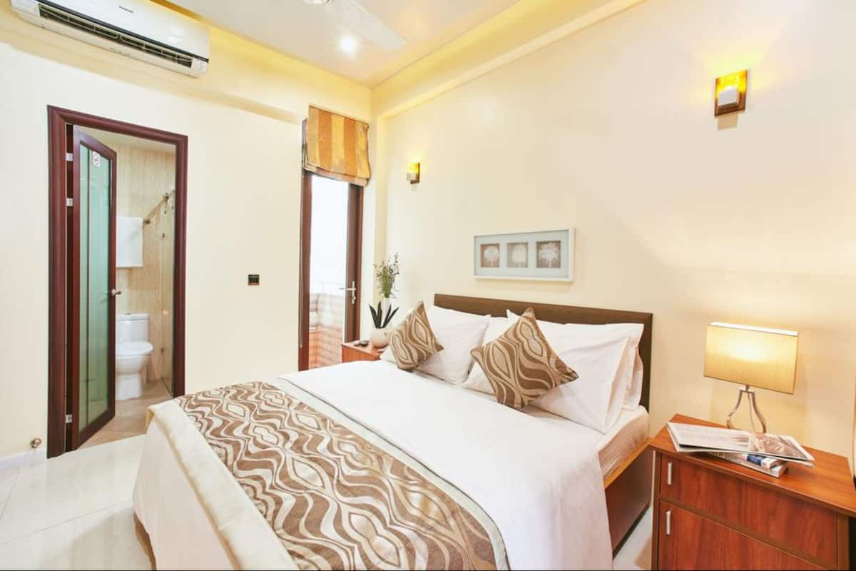 Habitación de hotel con una cama grande, una mesita de noche con lámpara, un tocador y una lámpara de pared.