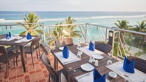 A terrace with tables set for dining, overlooking a beach with palm trees and the ocean. - Lonuveli (Hulhumalé)