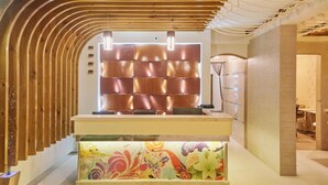 A reception area with a wooden slat wall, a cushioned seating area, and a colorful floral display. - Lonuveli (Hulhumalé)