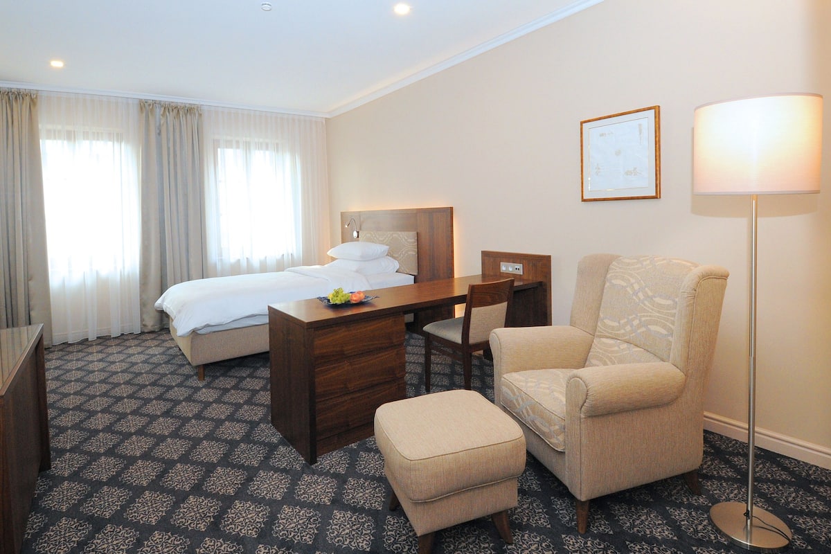 Una habitación de hotel con cama, escritorio, silla, lámpara y piso alfombrado.