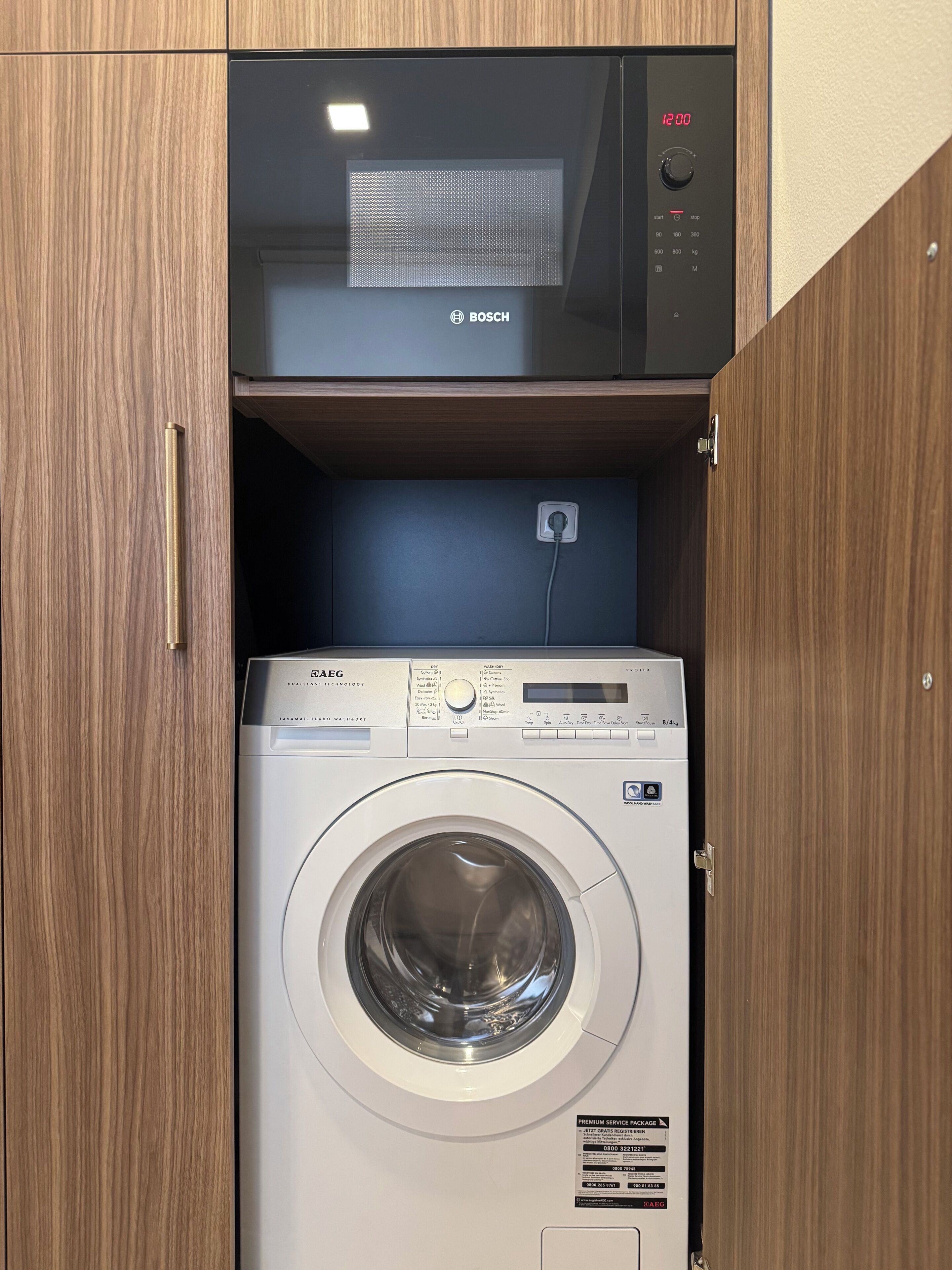 Een Bosch magnetron boven een SAEG wasmachine in een houten kast.