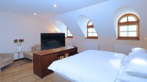 Ein Schlafzimmer mit einem großen Bett, einem Fernseher auf einem Holzboden, einem kleinen Tisch mit Blumen und bogenförmigen Fenstern.