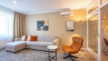 Een moderne woonkamer met een hoekbank, een fauteuil, een bijzettafeltje en een groot raam met gordijnen.