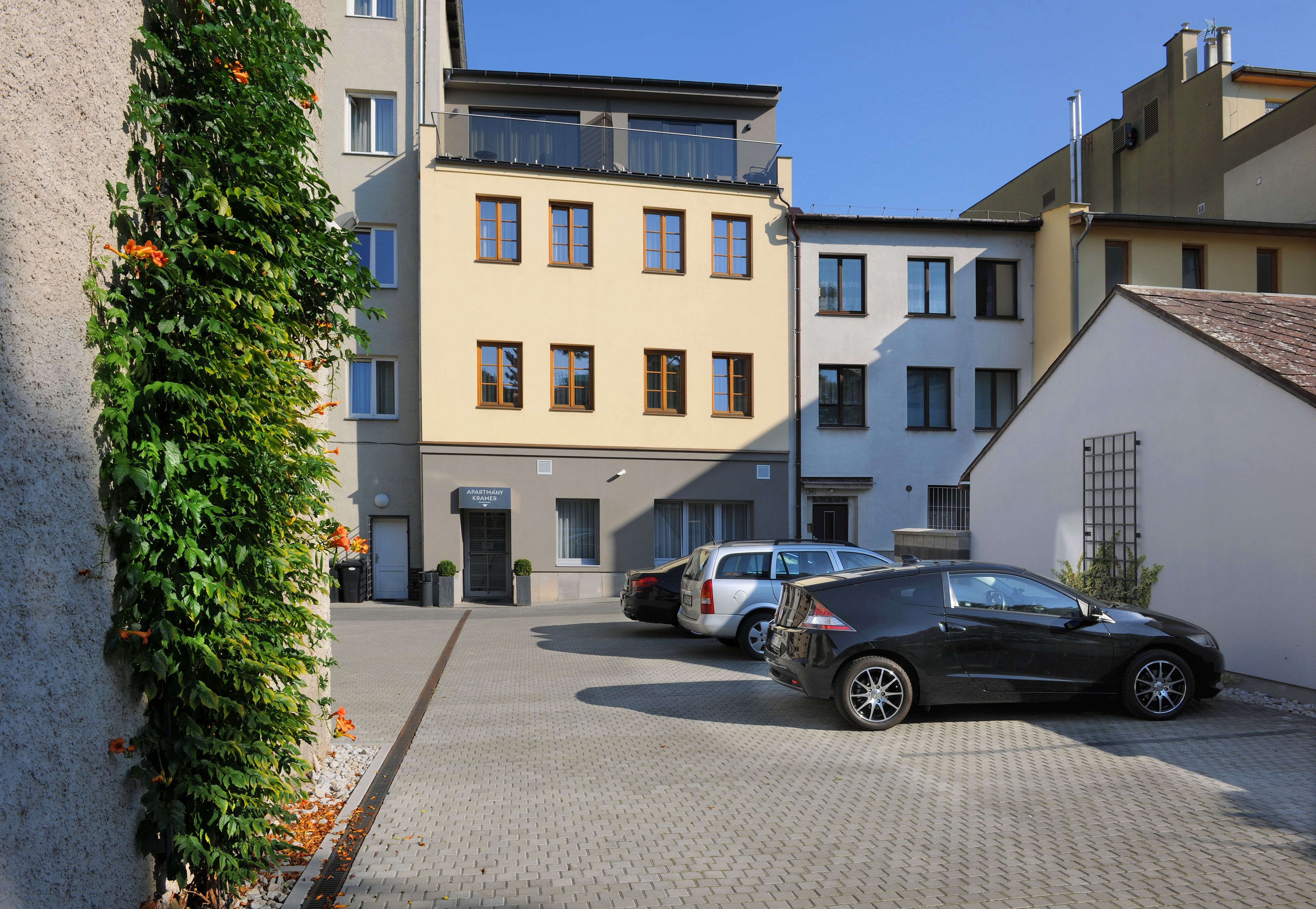 Un’area di parcheggio con due auto, un edificio con molte finestre e un muro ricoperto di piante rampicanti.