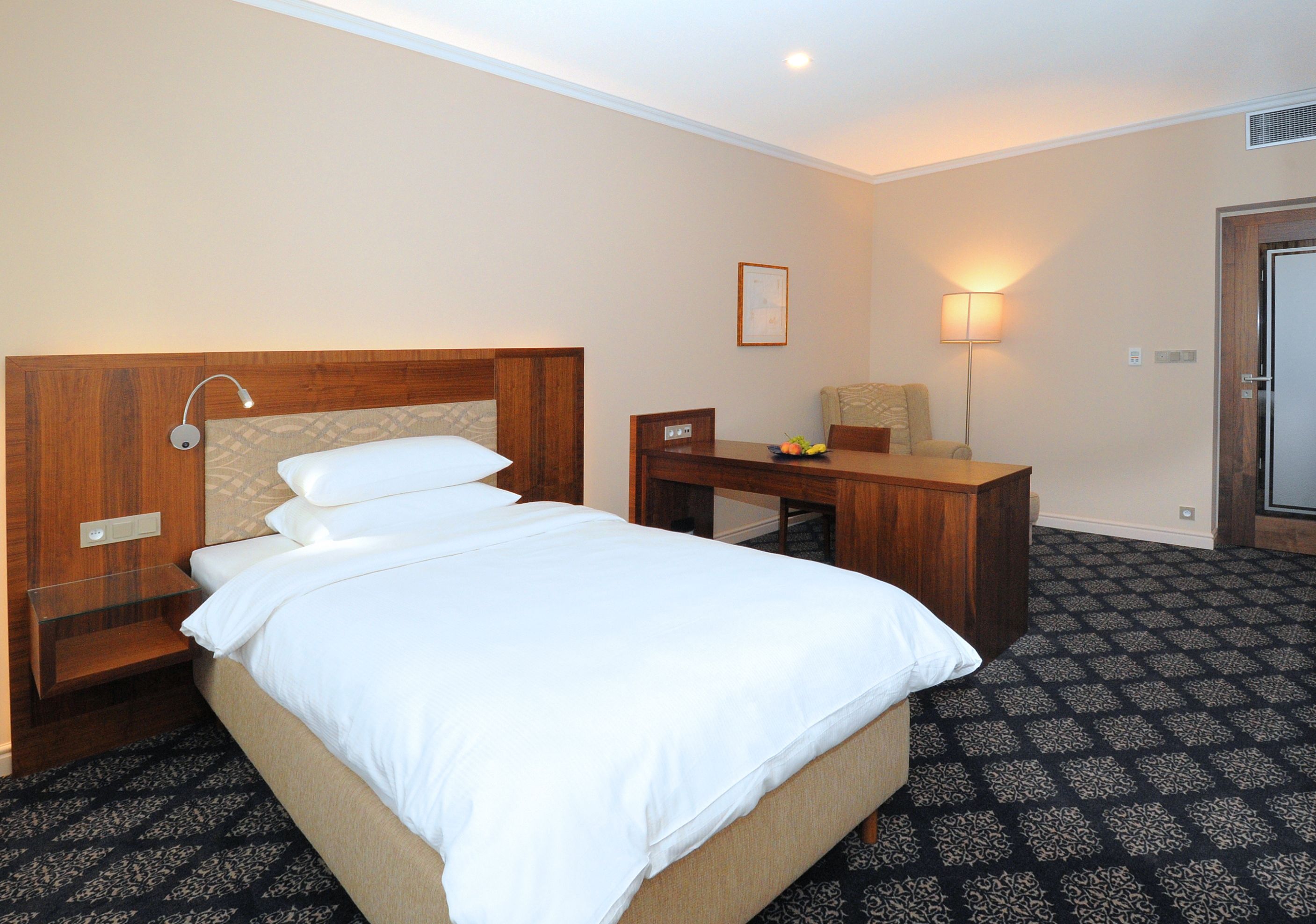 Una habitación de hotel con una cama, un escritorio, una silla, una lámpara y una puerta.