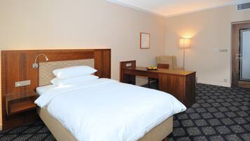 Una habitación de hotel con una cama, un escritorio, una silla, una lámpara y una puerta.