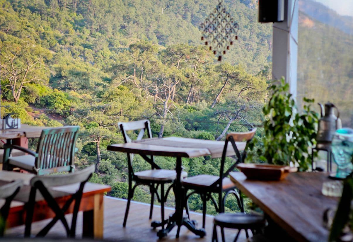 Terraço com mesa e cadeiras com vista para um morro arborizado.