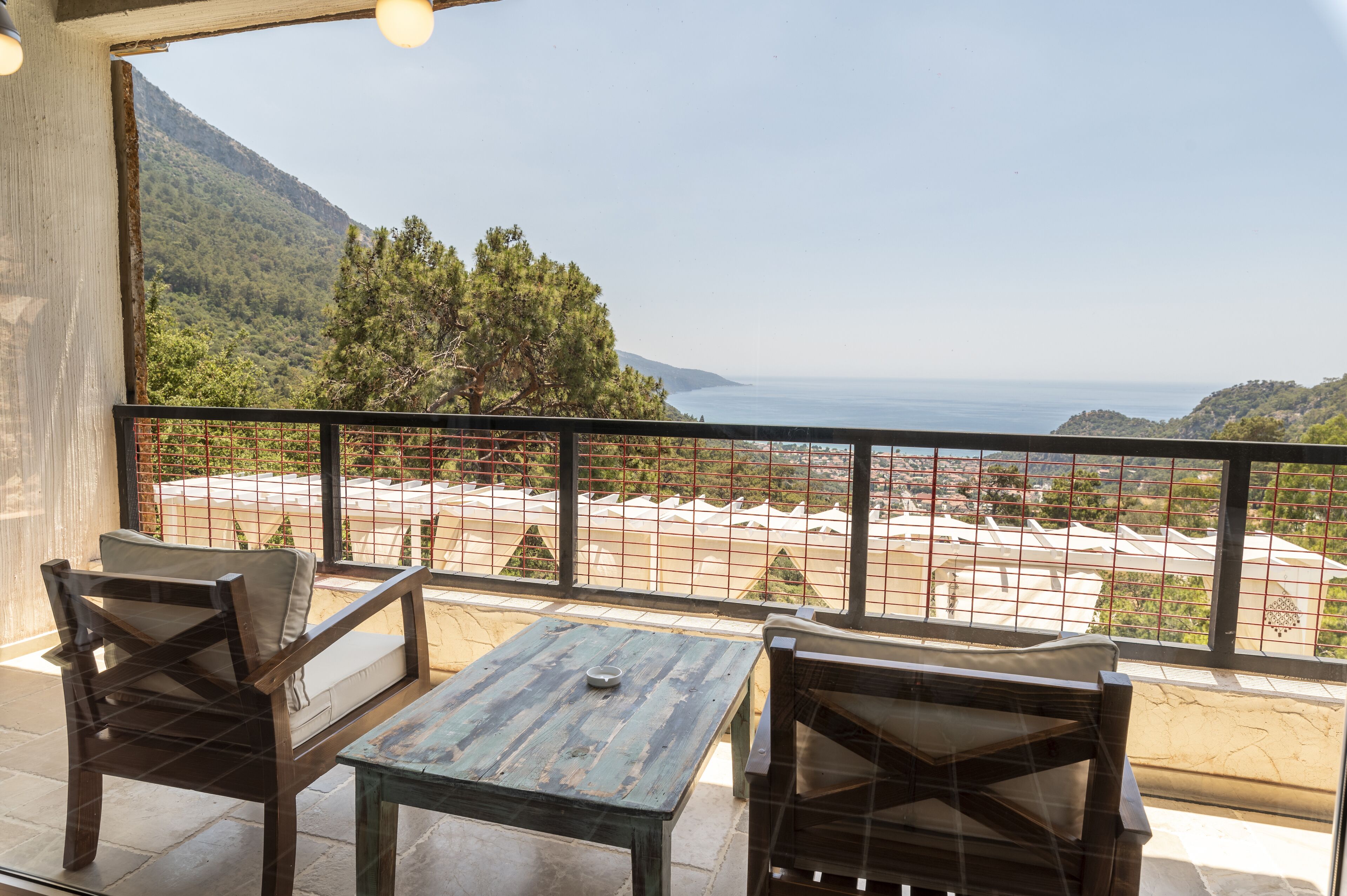 Un balcón con dos sillas de madera y una mesa, con vistas a un paisaje costero con árboles y al mar.
