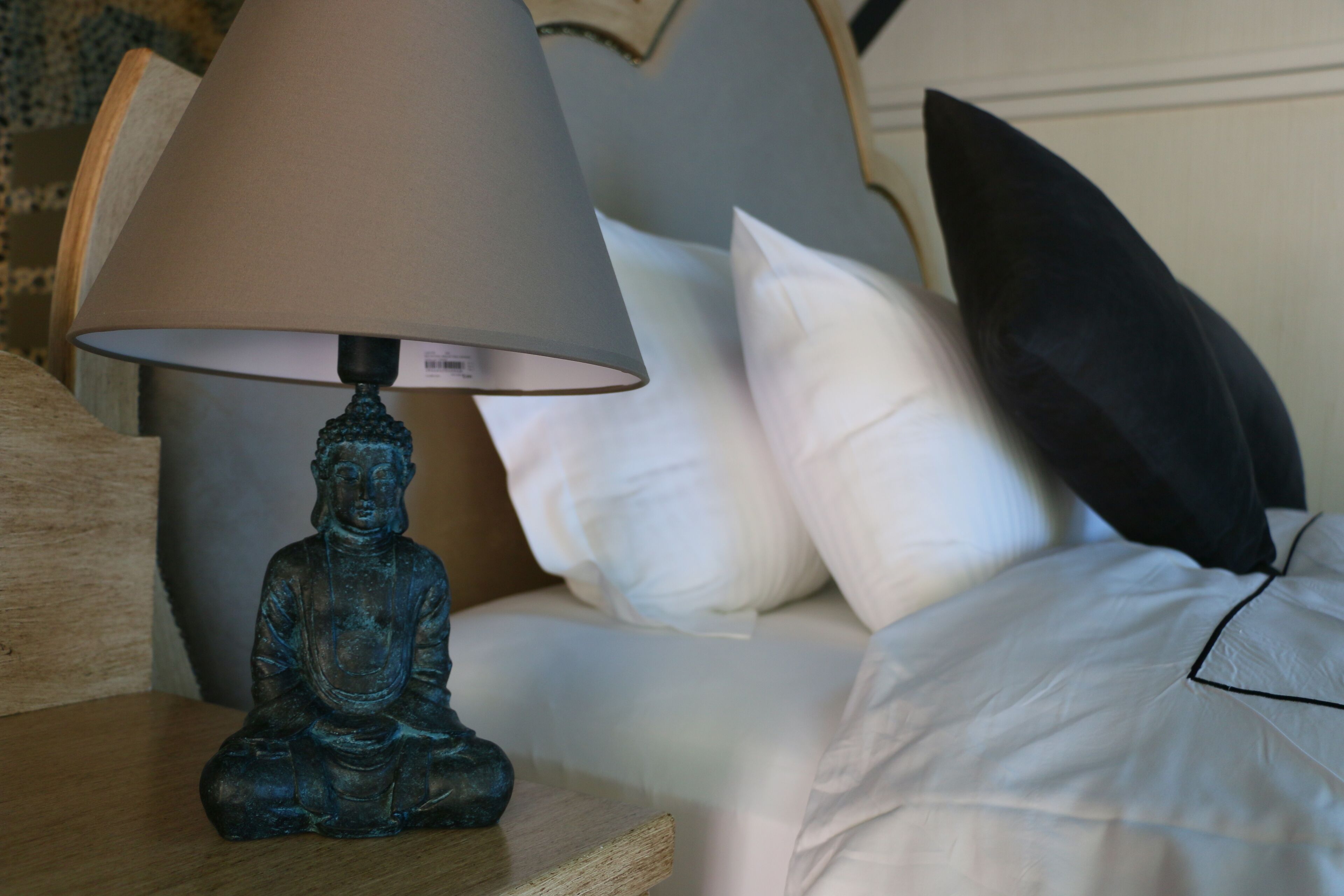 A bed with white pillows and a decorative Buddha statue on a bedside table.