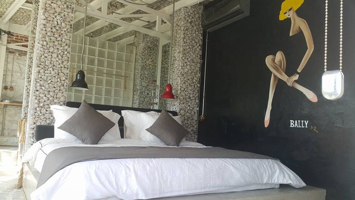 A bed with white bedding and gray pillows, a red pendant lamp, and a wall with a mural.