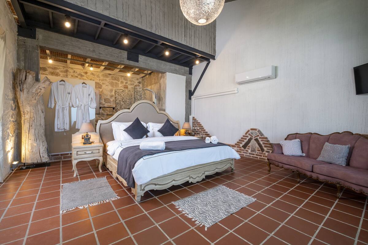 A bedroom with a bed, nightstands, a sofa, and a stone wall.
