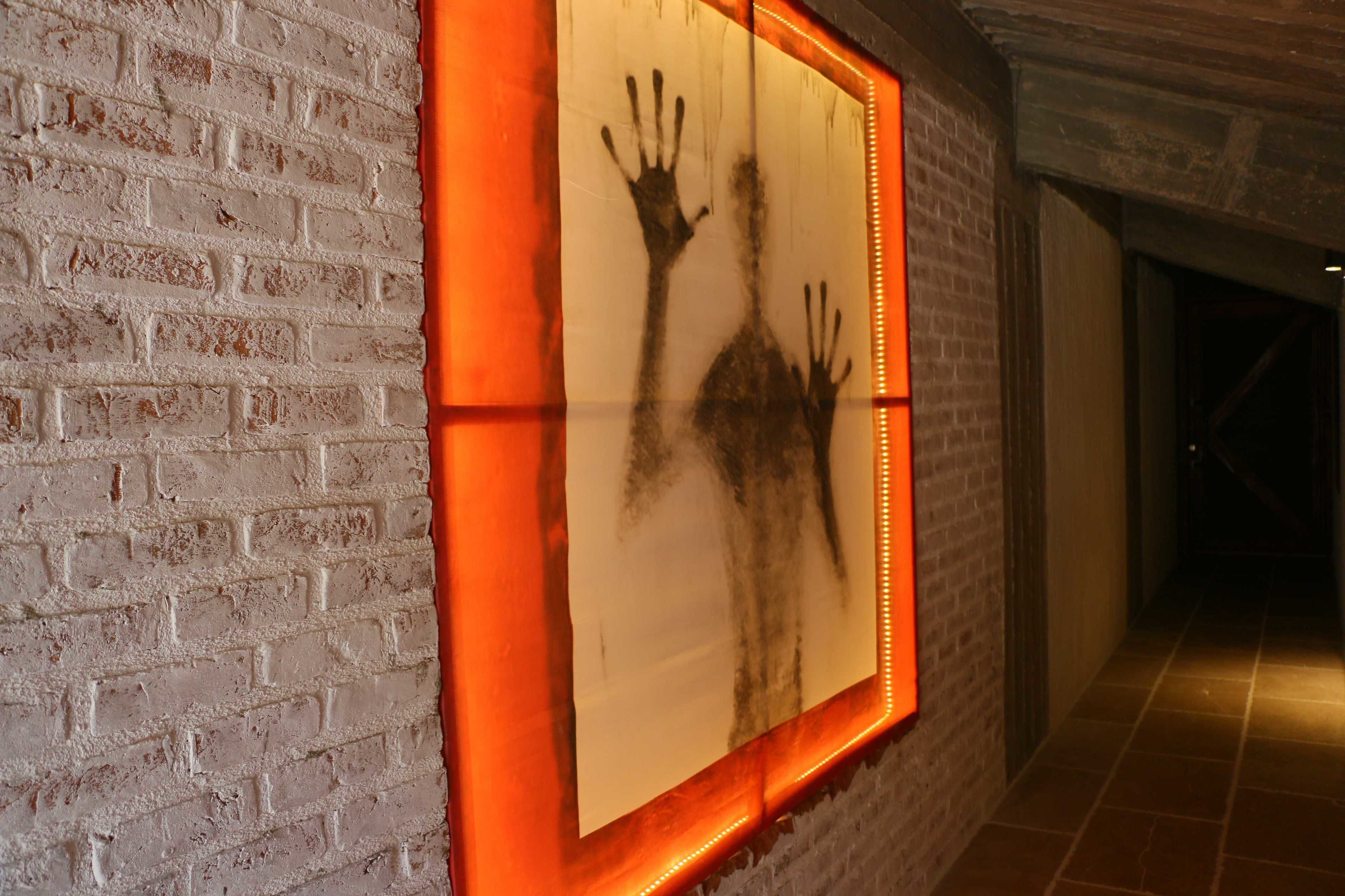 A hallway with a brick wall and a framed artwork featuring handprints.