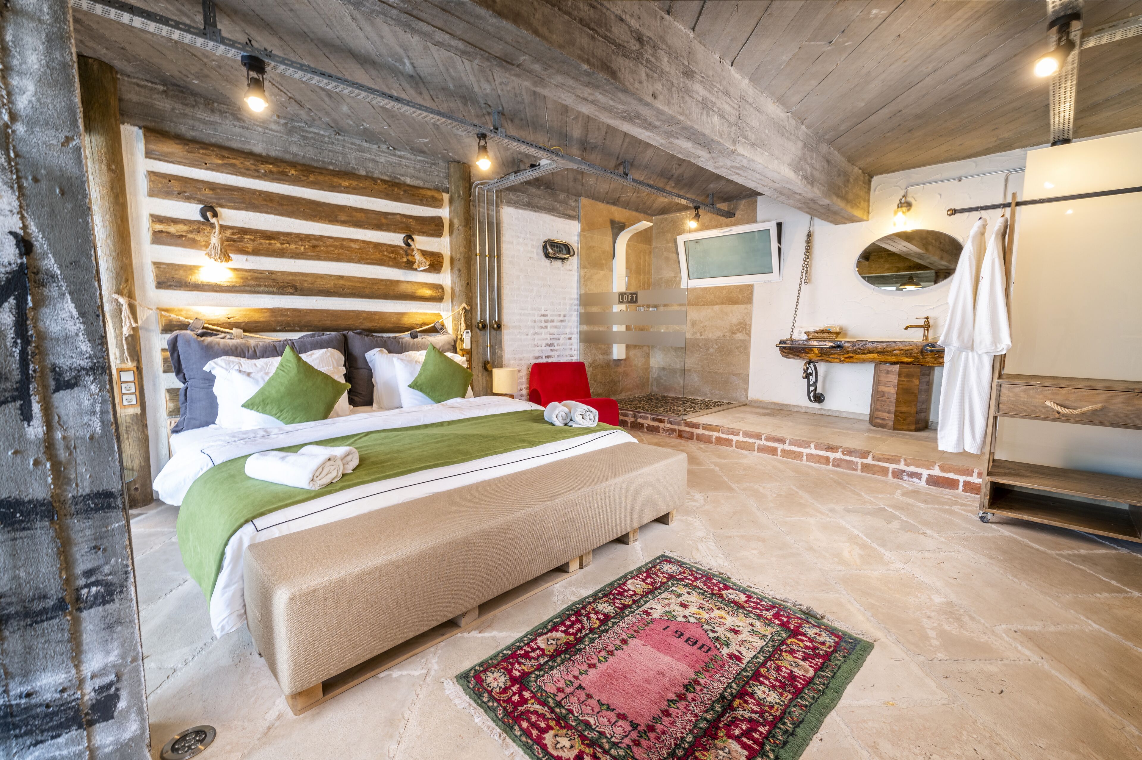 A bedroom with a bed, a red chair, a wooden dresser, a TV, and a bathroom with a mirror and sink.