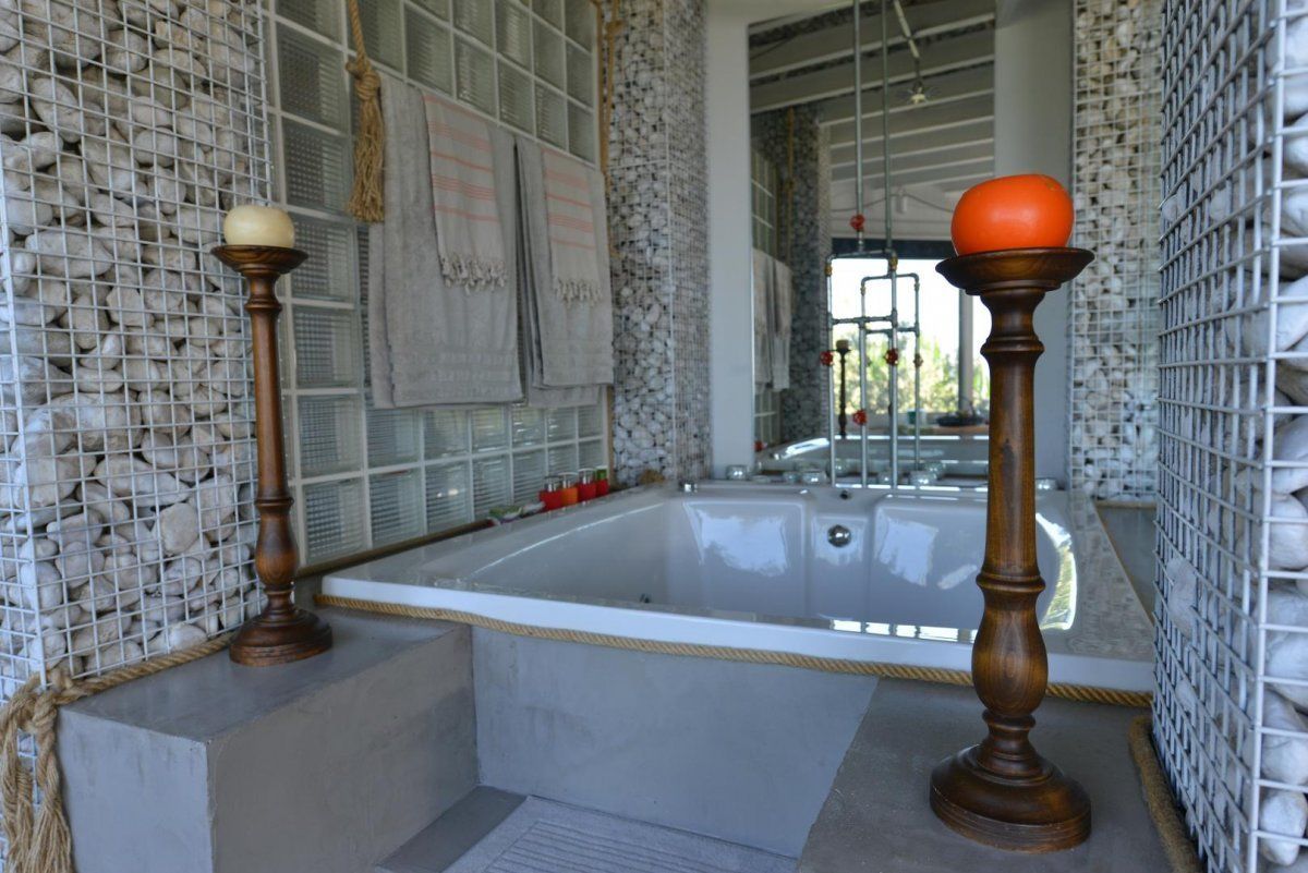 A modern bathroom with a large bathtub, stone wall decor, and wooden columns.