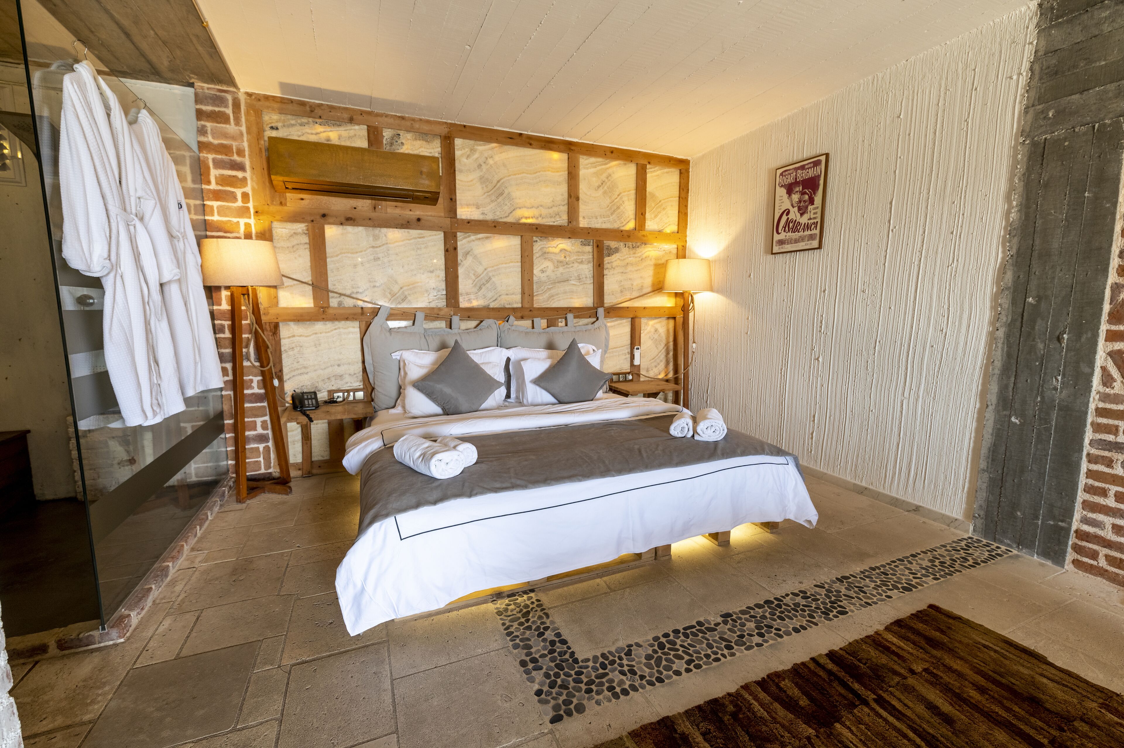 Une chambre avec un grand lit, deux tables de chevet, une cabine de douche en verre et un mur en briques.