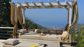 Eine Liege mit Meerblick, eine Pergola mit Vorhängen und ein Pool.