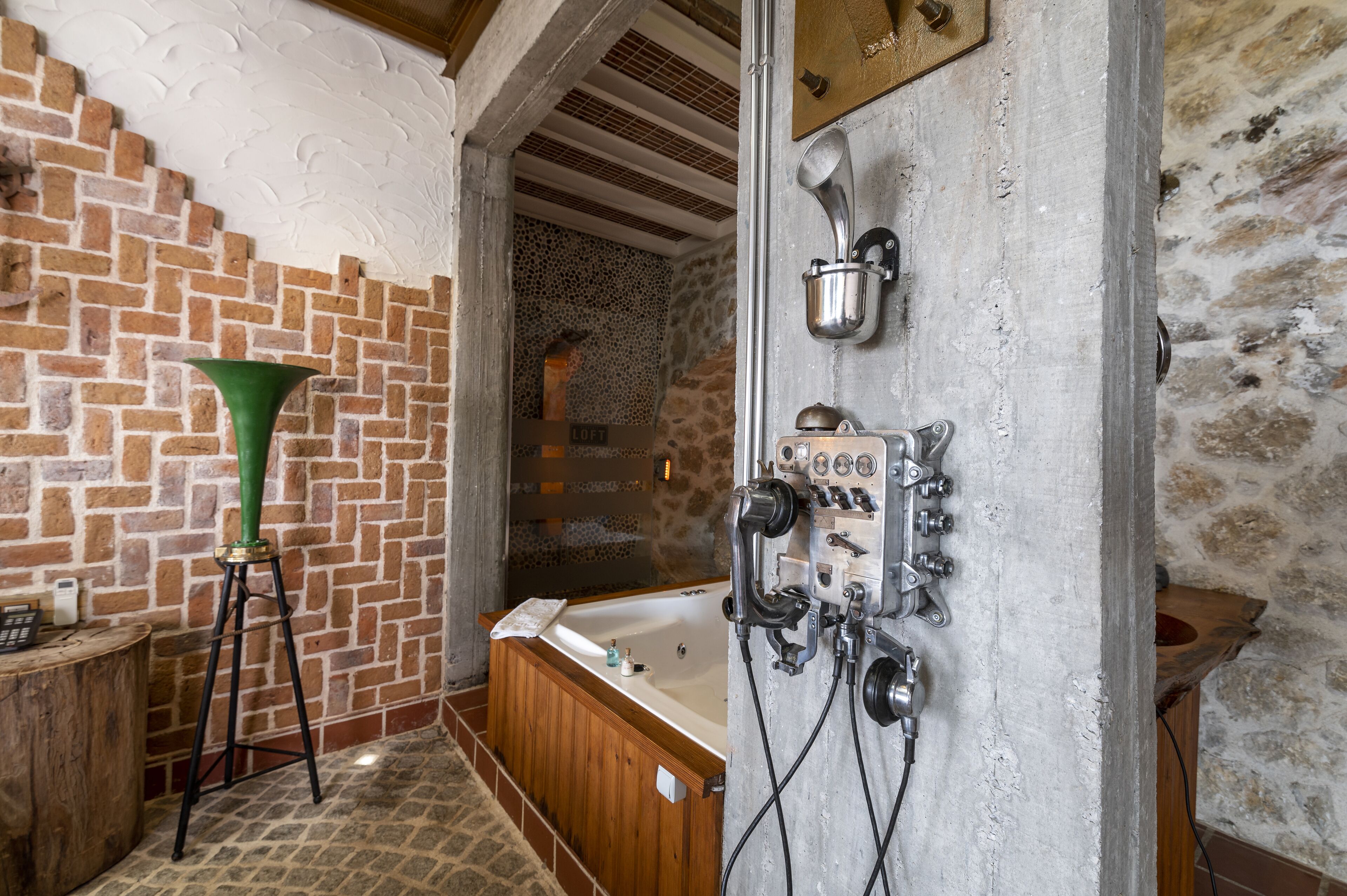 A bathroom with a wooden bathtub, a green vase, and a shower area with a stone wall.