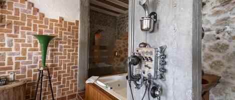 A bathroom with a wooden bathtub, a green vase, and a shower area with a stone wall.