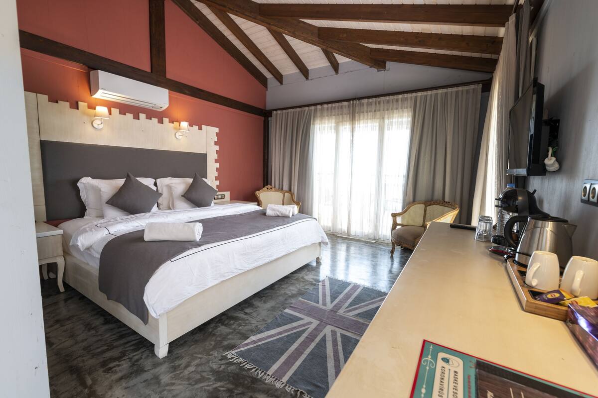 A bedroom with a large bed, bedside tables, a desk with a kettle, and a TV.