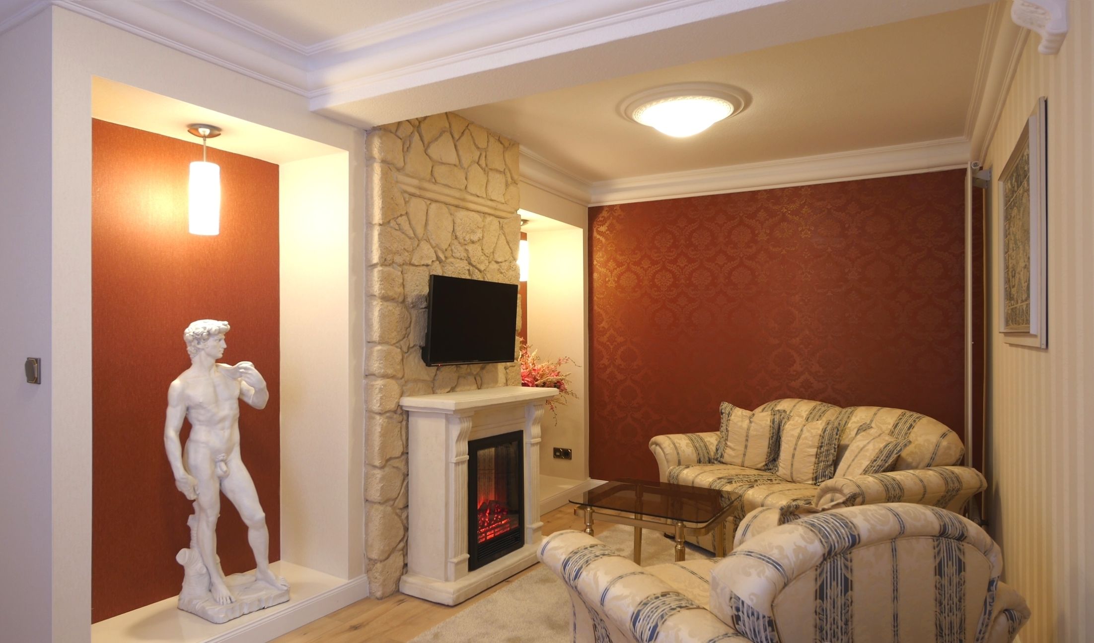 Una sala de estar con chimenea, un televisor montado en la pared y una estatua de figura clásica.