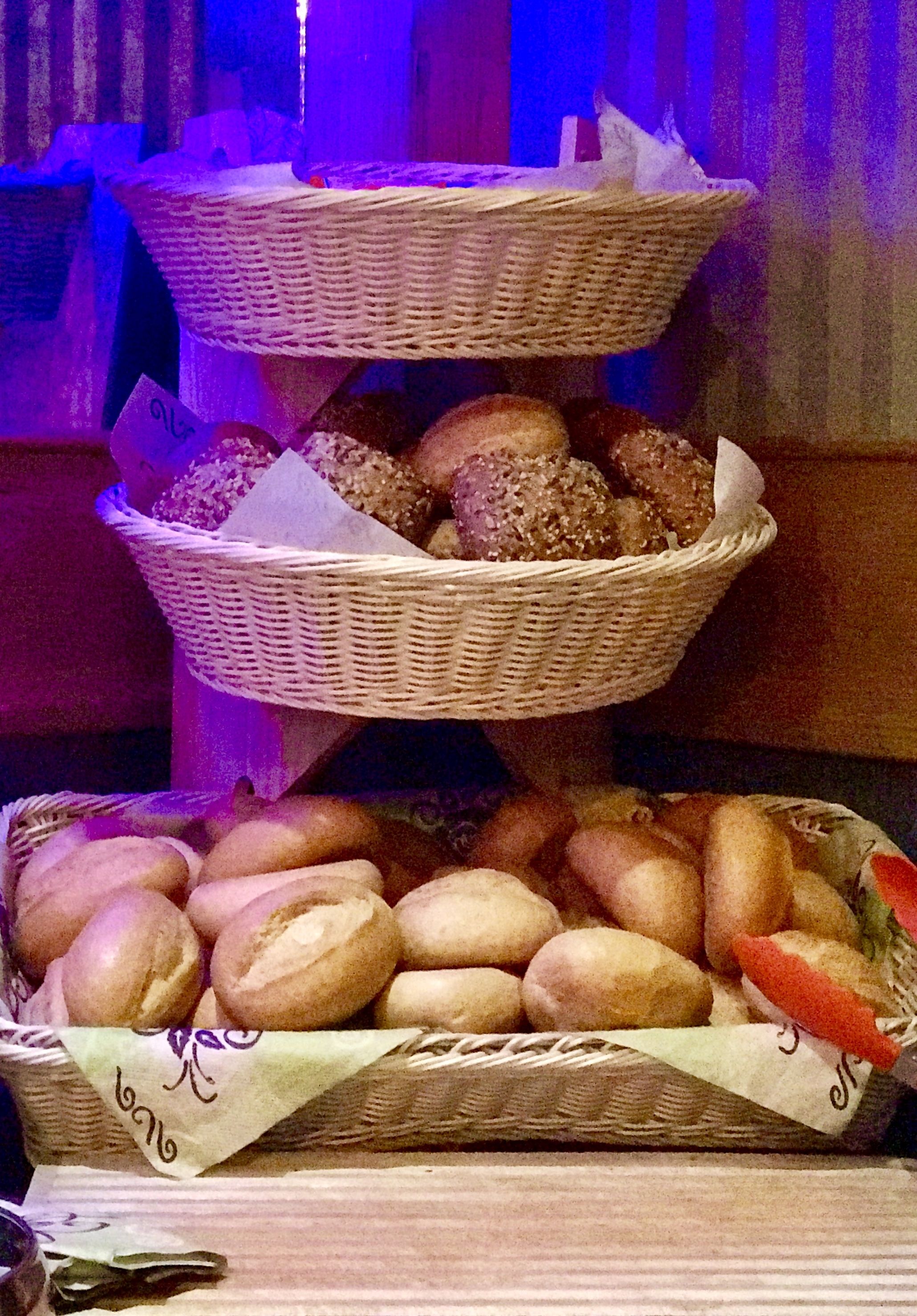 A three-tiered display of baked goods, including bread and pastries, arranged on a table.