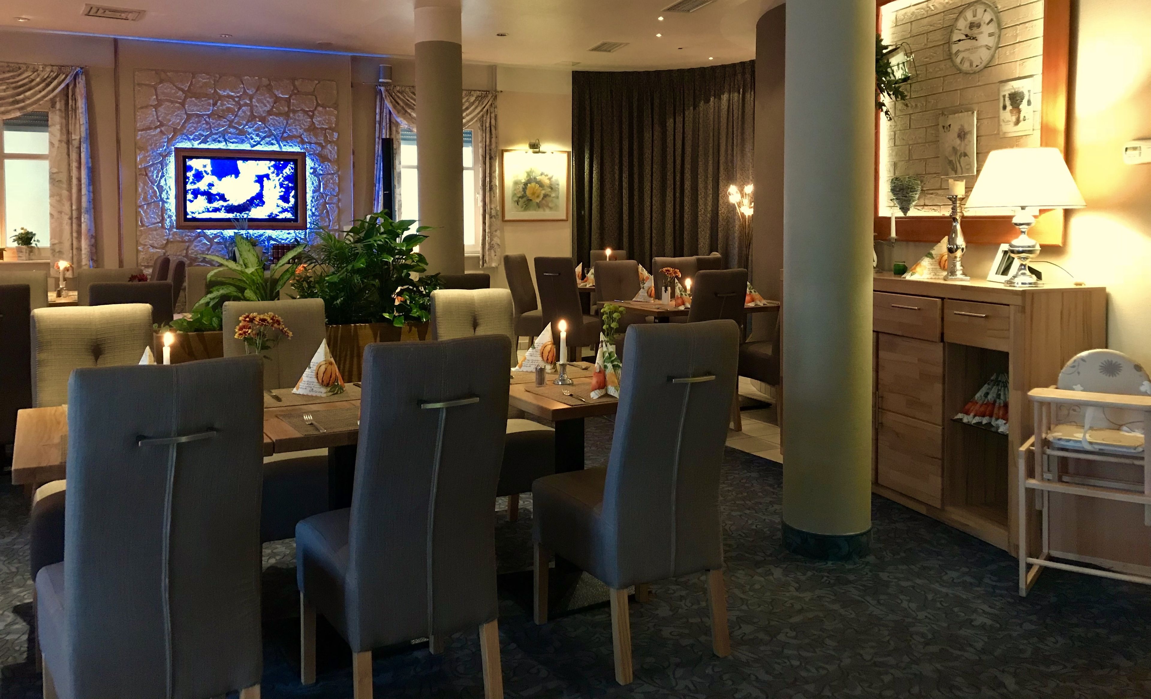 A hotel dining area with a television, dining tables, chairs, and a kitchen area.