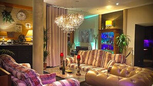 Un salón luminoso con un conjunto de sofás, una araña y una zona de bar con botellas.