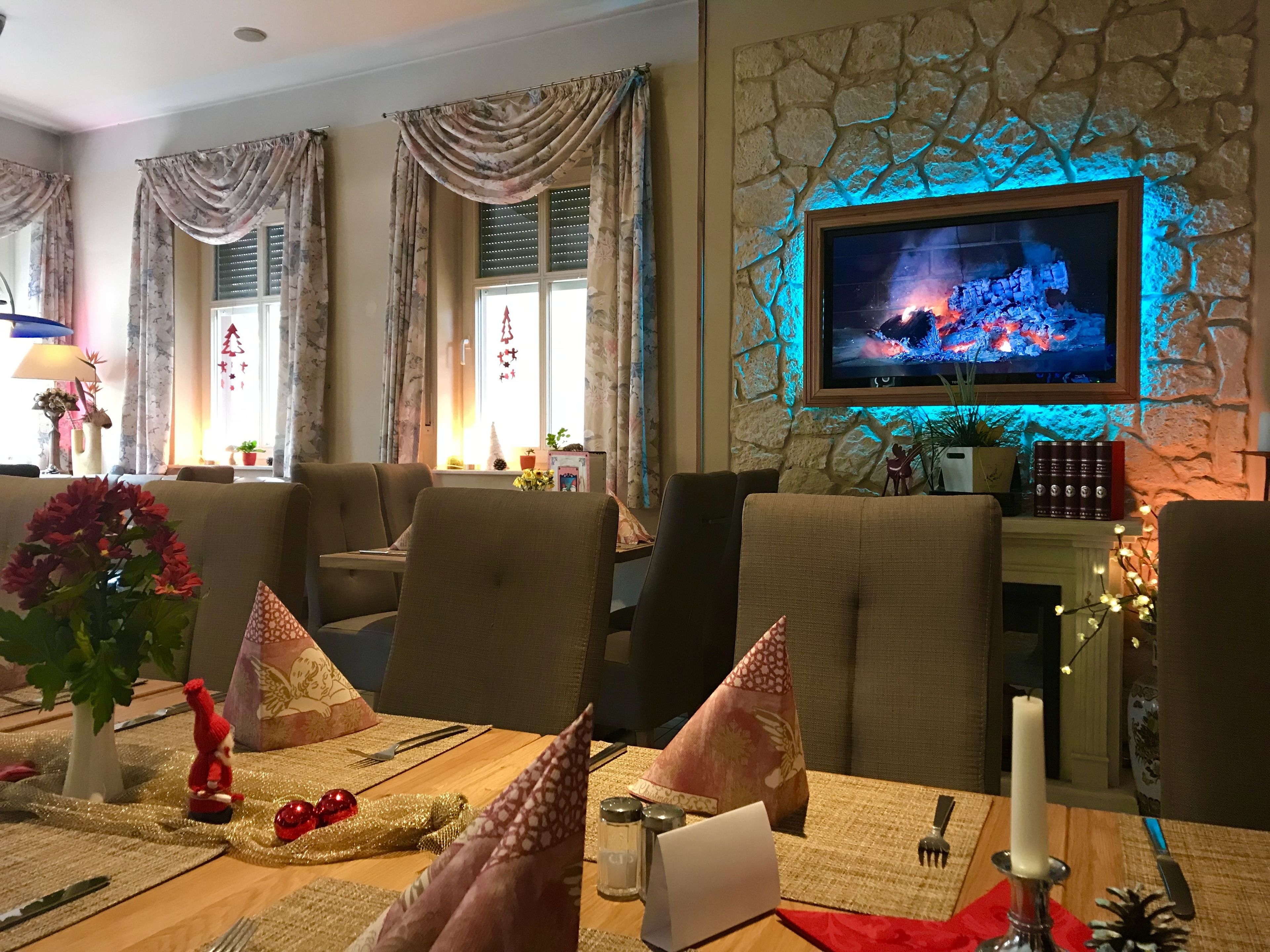 Un área de comedor con pared de piedra, un televisor montado sobre la chimenea, y una mesa decorada con una vela, una figura pequeña de Santa Claus y un adorno rojo.