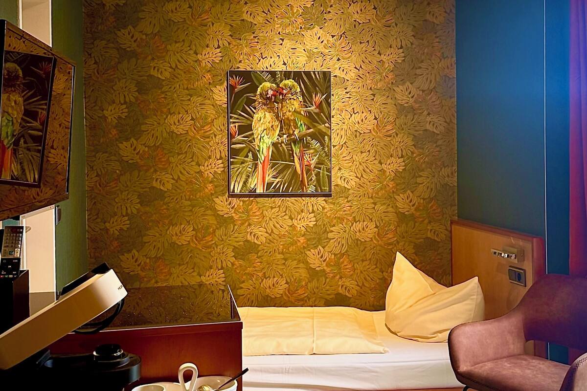Ein Hotelzimmer mit Bett, Schreibtisch, Computer, Lampe, Stuhl und einem Bild an der Wand.