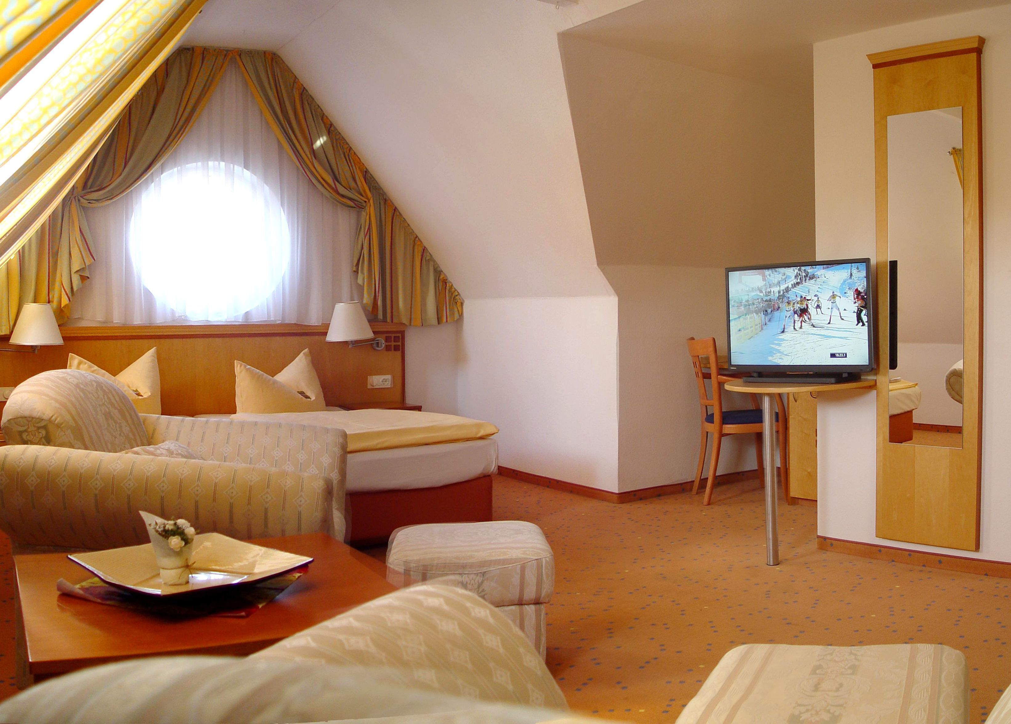 Ein Hotelzimmer mit einem Bett, einem Schreibtisch mit Fernseher, einem Sessel und einem kleinen Tisch mit einer Dekoration.