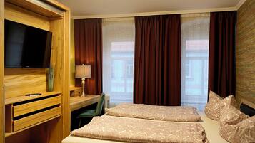 Habitación de hotel con televisor, escritorio, dos camas y ventanas amplias con cortinas.