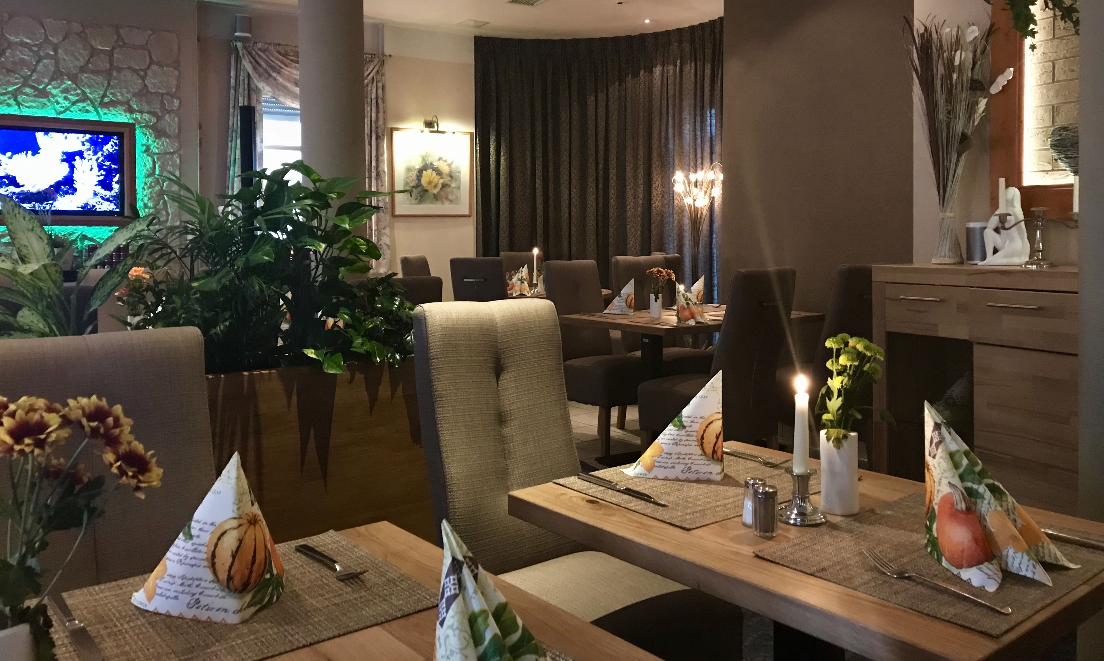Een eetgedeelte met tafels voor twee personen, voorzien van placemats met pompoenmotieven, kaarsen en een vaas met bloemen.