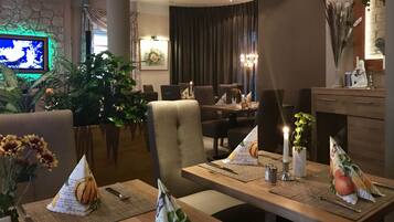 Een eetgedeelte met tafels voor twee personen, voorzien van placemats met pompoenmotieven, kaarsen en een vaas met bloemen.