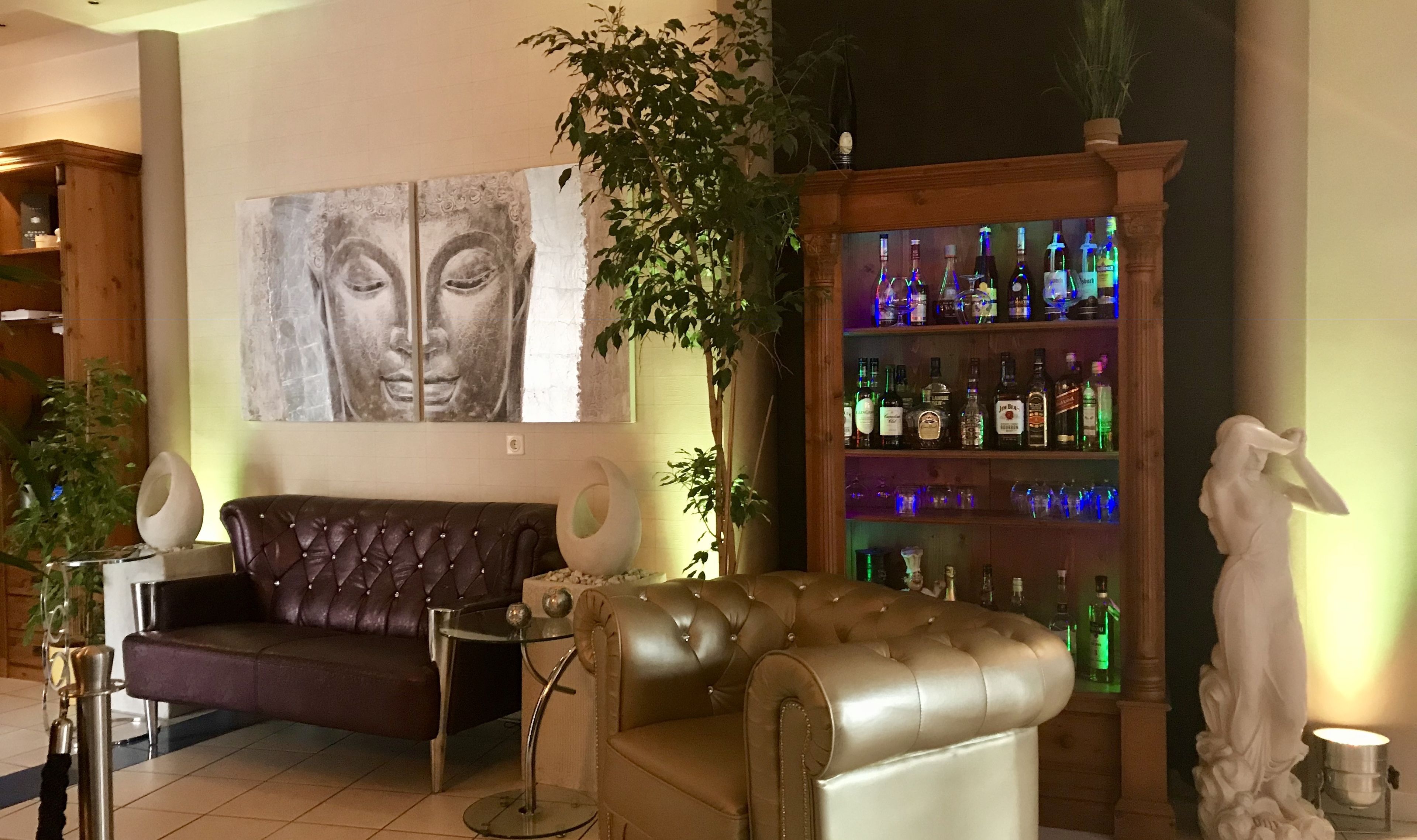 Een hal met een leren bank, een glazen bijzettafeltje, een groot Boeddha-schilderij, een plant, een beeld en een bar met flessen.