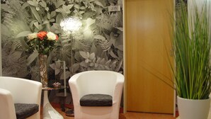 Una habitación con un sillón blanco, una mesita con un florero y una planta grande en maceta.