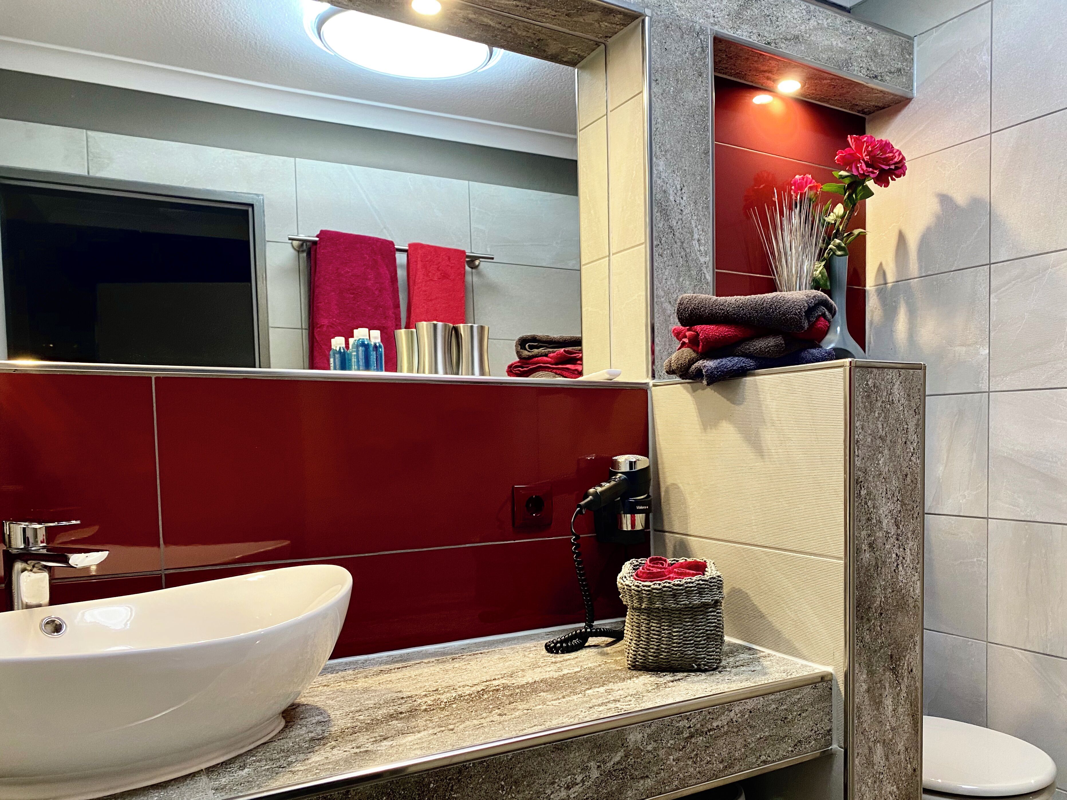 Un baño moderno con un lavabo blanco, toallas rojas y un espejo.
