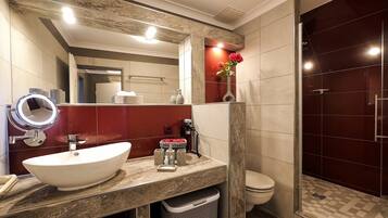 A modern bathroom with a white sink, a round mirror, a red accent wall, a toilet, and a shower area.
