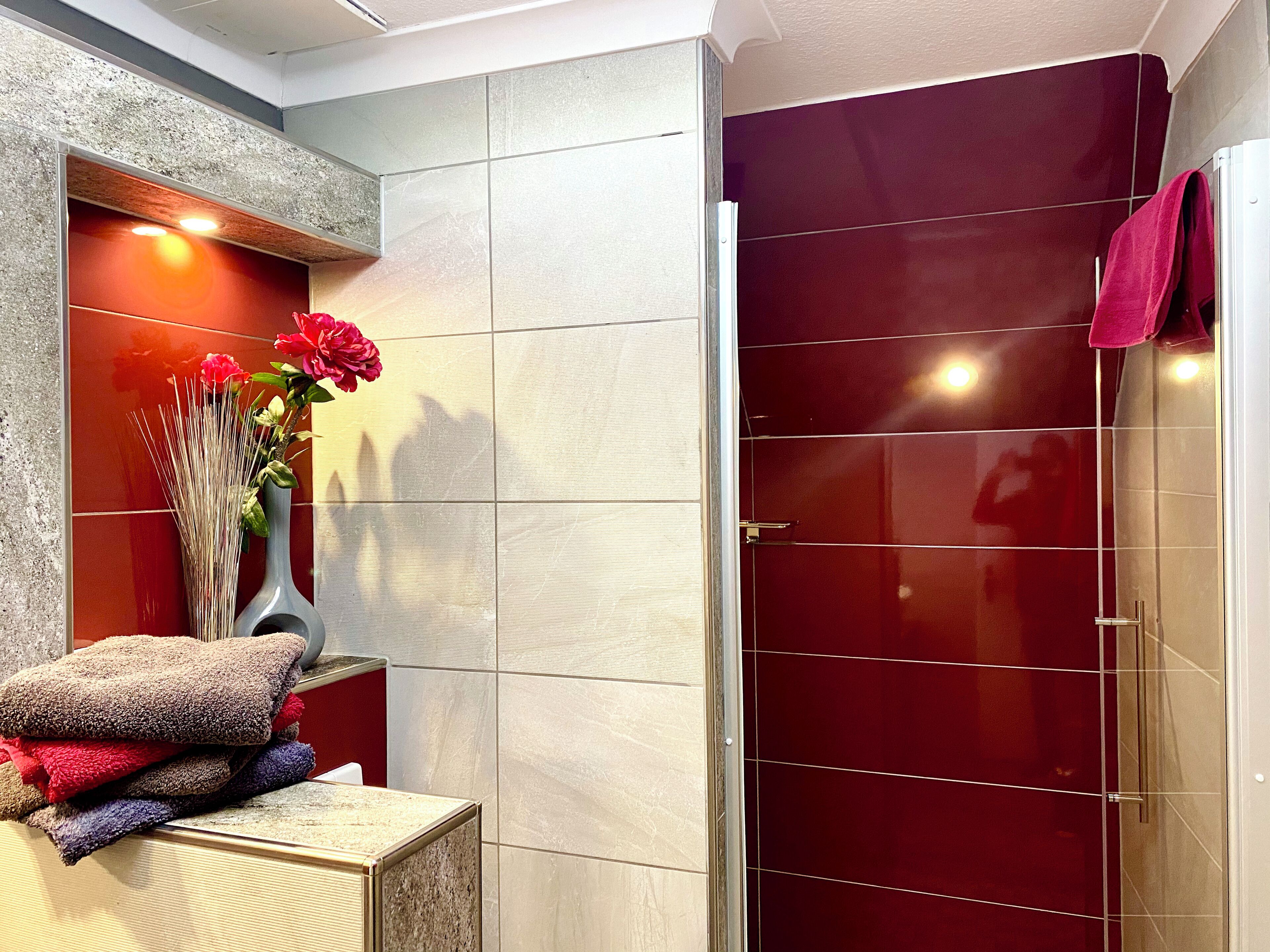 A bathroom with a glass shower door, a marble sink, and a vase with flowers.