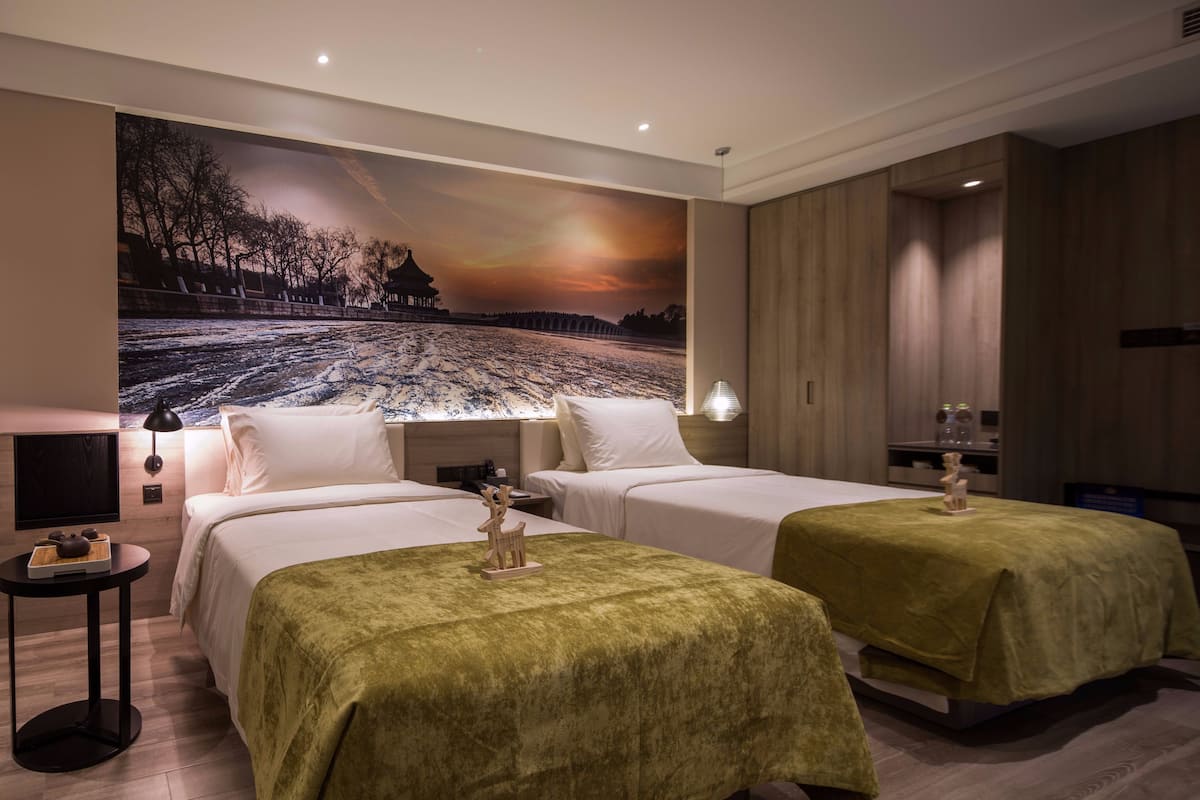 Habitación de hotel con dos camas, un mural grande en la pared, una mesita con juego de té y una mesita de noche con lámpara.