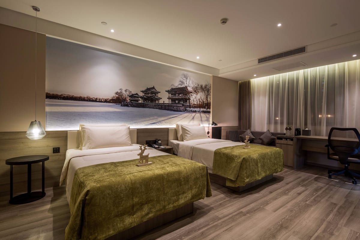 Habitación de hotel con dos camas, un escritorio, una silla y un mural grande de una edificación tradicional.