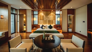 Una habitación de hotel moderna con una cama grande, dos mesitas de noche, una mesa redonda de centro con un jarrón y una tetera, y dos sillones.