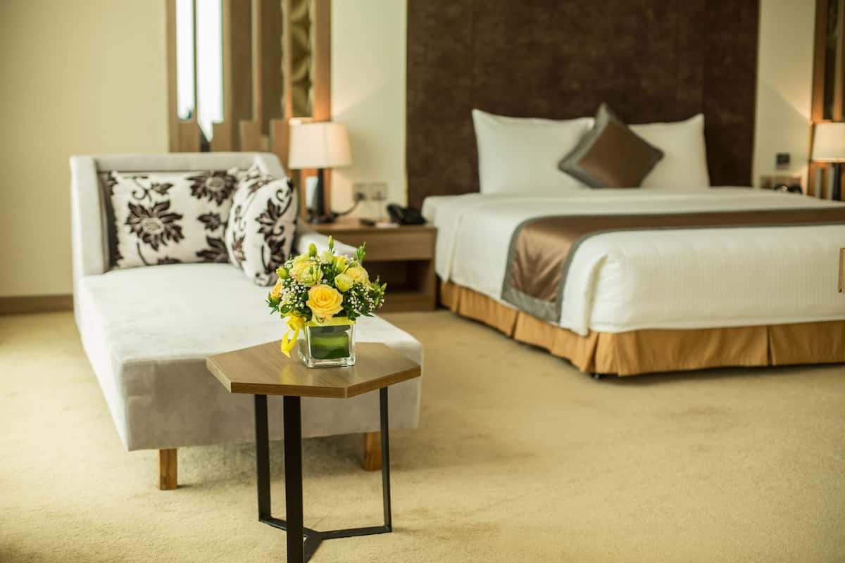 A hotel room with a bed, a sofa, a small table with a vase of flowers, and two bedside lamps.